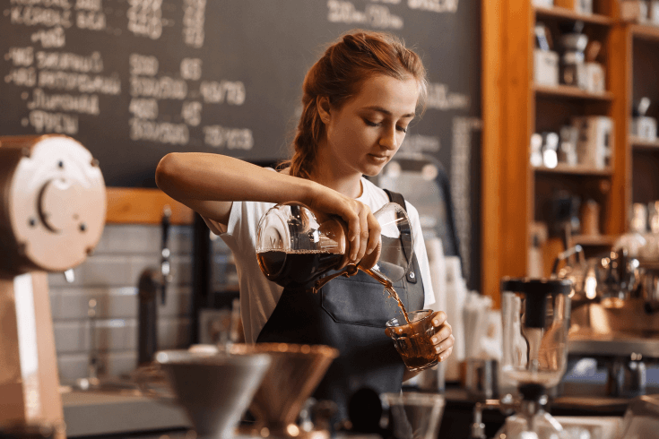 A female barista preparing coffee behind the counter in a cafe.