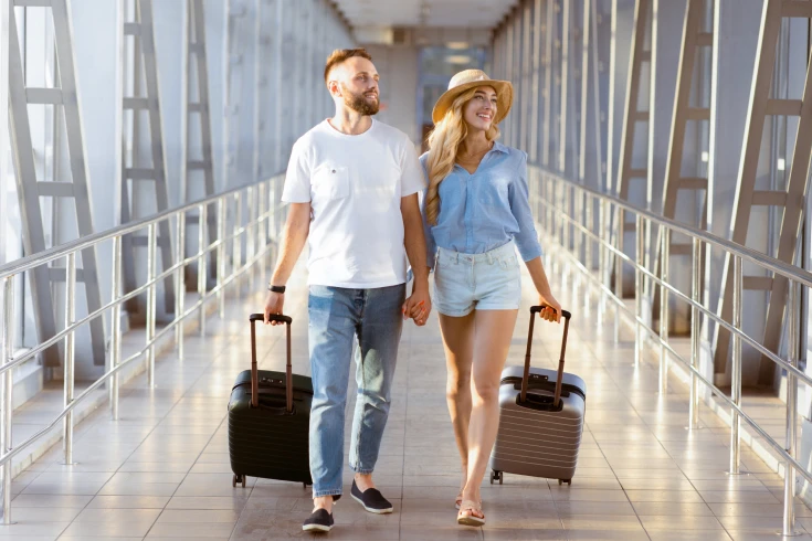 Male and female couple walking through airport with suitcases