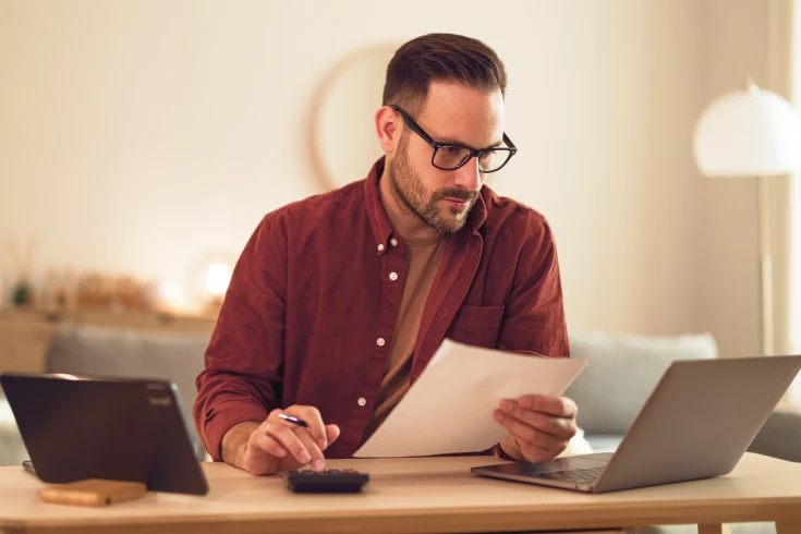 An image of a person looking at a laptop and crunching numbers