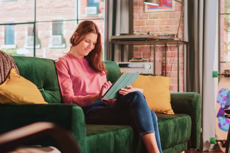 Woman sitting on green couch in home using a tablet/ipad