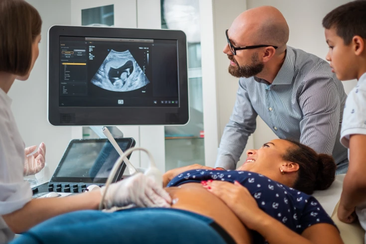 Woman having a pregnancy ultrasound with her husband and son next to her