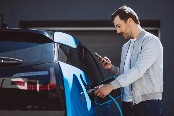 Man looking at his phone while plugging a charger into his electric vehicle (EV)